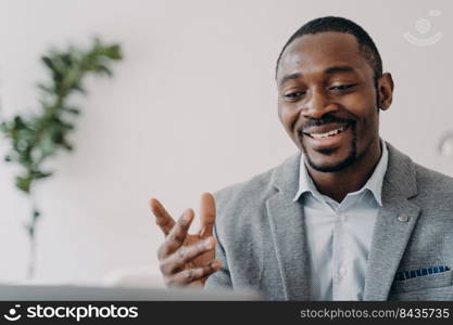 Smiling african american businessman holding a video call with customers on laptop. Optimistic black male businessperson or coach gives online consultation, advises clients.. Smiling african american businessman holding a video call with customers on laptop, advises clients