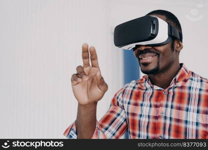 Smiling african american man using virtual reality glasses touch objects, interact with cyberspace, happy black guy in VR goggles playing online video game. Technology, entertainment.. African american man in virtual reality glasses, interact with cyberspace, play online video game