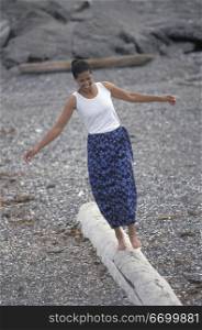 Smiling African American Woman Balancing On A Log On A Rocky Beach