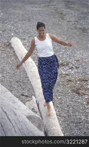 Smiling African American Woman Standing On A Log On A Rocky Beach