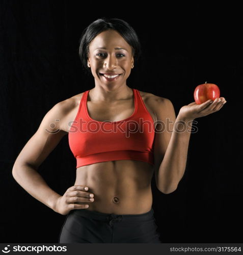 Smiling African American young adult woman holding apple with hand on hip.