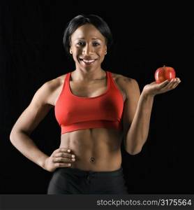 Smiling African American young adult woman holding apple with hand on hip.
