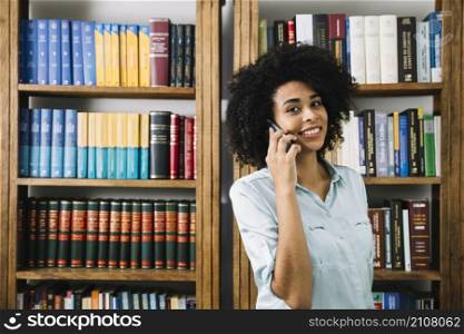 smiling african american young lady talking smartphone near books