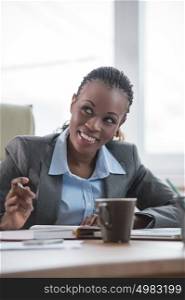 Smiling african businesswoman in formalwear sitting at workplace and planning
