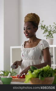 Smiling african woman chopping vegetables for salad at kitchen