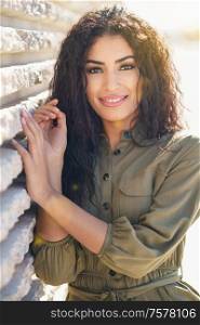 Smiling Arab Woman with curly hair in urban background. Young Arab Woman with curly hair outdoors