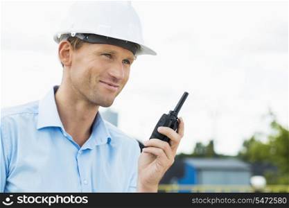 Smiling architect holding walkie-talkie at construction site
