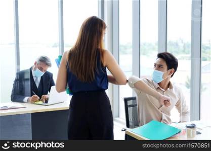Smiling Asain businessman and businesswoman greeting with colleagues bumping elbows for preventing covid 19 virus in workspace at office. Social distance and new normal lifestyle concept.