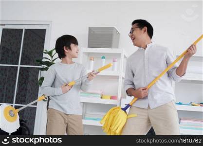 Smiling Asian father and little boy child is enjoying for House cleaning together in Laundry room. They singing with mop for play guitar on holiday.