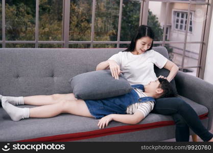 Smiling Asian mother and little girl child is relaxing and laying together on sofa in living room. Family time for mom and daughter Concept