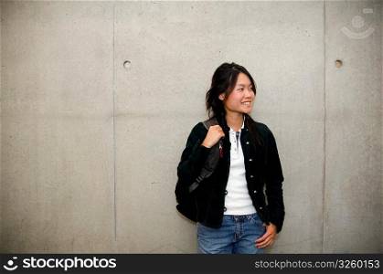 Smiling Asian student leaning on school cement wall.