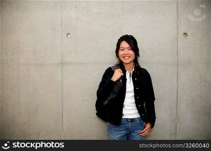 Smiling Asian student standing against cement wall.