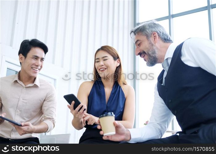 Smiling Asian team and Senior Caucasian businesspeople teamwork relaxing and brainstorm. Businesswoman holding smartphone and talking together at office. Focus asian woman.