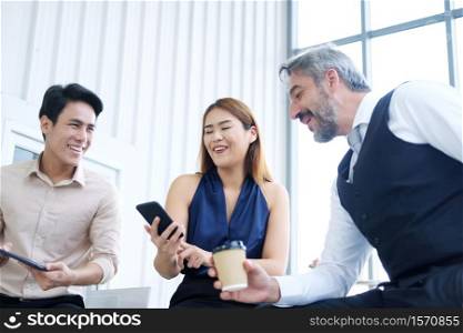 Smiling Asian team and Senior Caucasian businesspeople teamwork relaxing and brainstorm. Businesswoman holding smartphone and talking together at office. Focus asian woman.