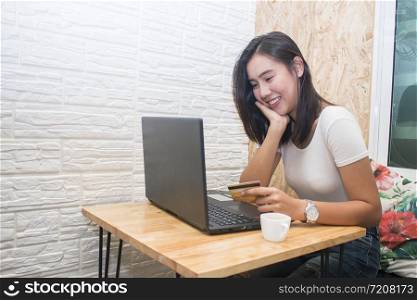 Smiling asian woman holding credit card and using laptop computer to shopping on line at cafe