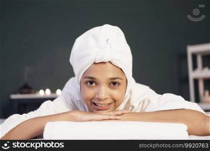 Smiling Asian woman in white headscarf and bath towel lie down on bed preparing for massage therapy at alternative medicine healing spa Center in Thailand