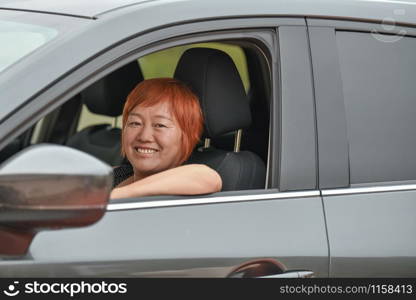 Smiling asian woman looking at camera while driving a gray car, travel concept.