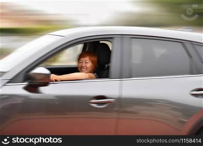 Smiling asian woman looking at the camera while driving a fast gray car, travel concept. Defocused and distorted background.