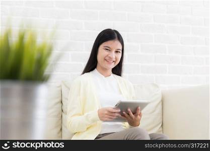 Smiling asian woman using tablet on sofa at home in the living room