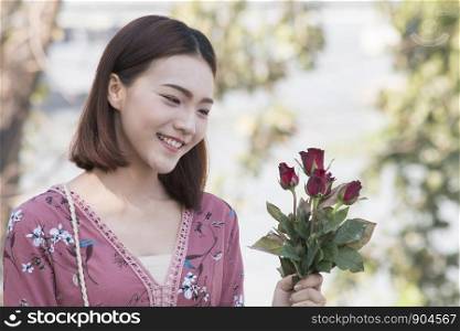 Smiling asian women seeing red roses at park