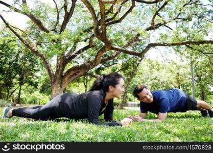 Smiling Asian young couples love exercising and planking workout together on grass field in the garden. Healthy and sport for relationship Concept