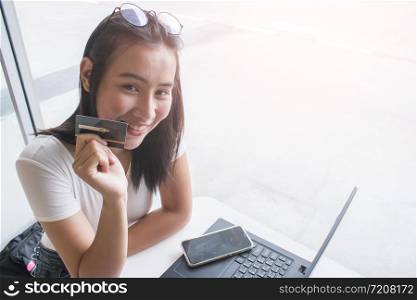 Smiling asian young female model holding up credit card.