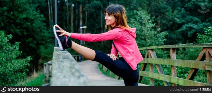 Smiling athlete woman doing leg stretch outdoors