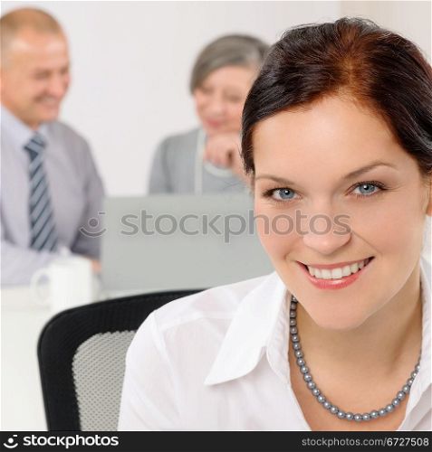 Smiling attractive businesswoman in office closeup with colleagues in background