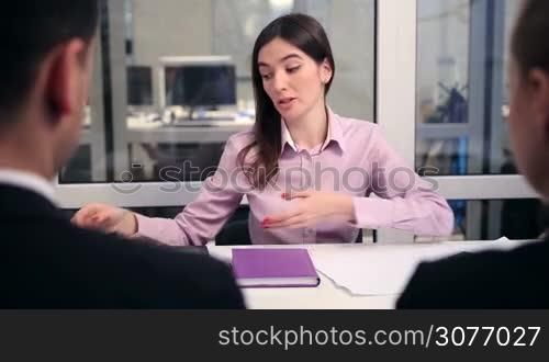 Smiling attractive female real-estate agent showing house plan to a young couple on touchpad at the office. Young woman signing contract with electronic signature on digital tablet computer in real estate office.