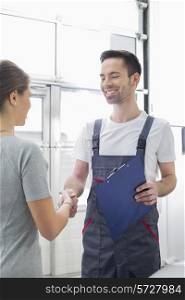 Smiling automobile mechanic shaking hands with female customer in automobile repair shop