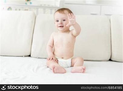 Smiling baby boy in diapers sitting on bed
