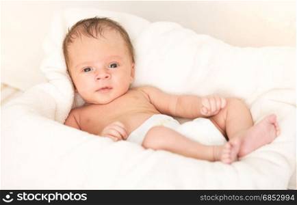 Smiling baby boy lying on soft beige blanket and cushion