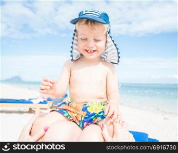 Smiling baby boy sitting at mom in her legs on the beach.
