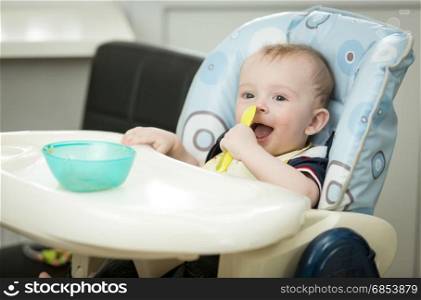 Smiling baby boy sitting in highchair and eating gruel from spoon