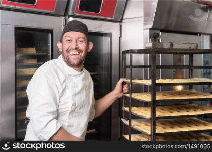 Smiling Baker putting a rack of pastries into the oven in bakery or pastry shop .. Smiling Baker putting a rack of pastries into the oven in bakery or pastry shop.