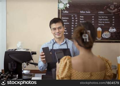 Smiling barista giving online payment to customer , pay for the order in a cafe shop