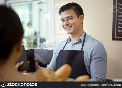 Smiling barista giving online payment to customer , pay for the order in a cafe shop