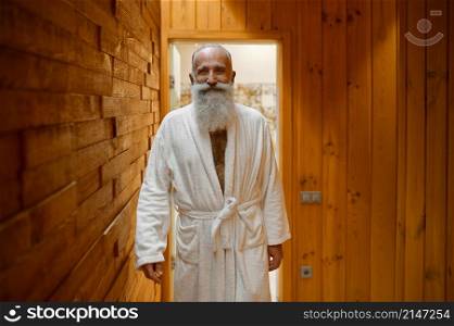 Smiling bearded man in bathrobe relaxing in wooden sauna room at spa resort looking at camera. Smiling bearded man in bathrobe in sauna