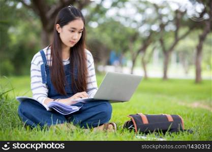 Smiling beautiful Asian girl reading book and working at tree on park in summer for relax time