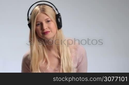 Smiling beautiful girl with earphones enjoying music on white background. Playful cheerful young woman wearing lipstick is listening to music on headphones, flirting to the camera and twisting the headphones wire around her finger.