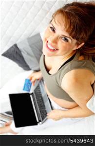 Smiling beautiful pregnant female on sofa at home with the laptop and credit card.&#xA;