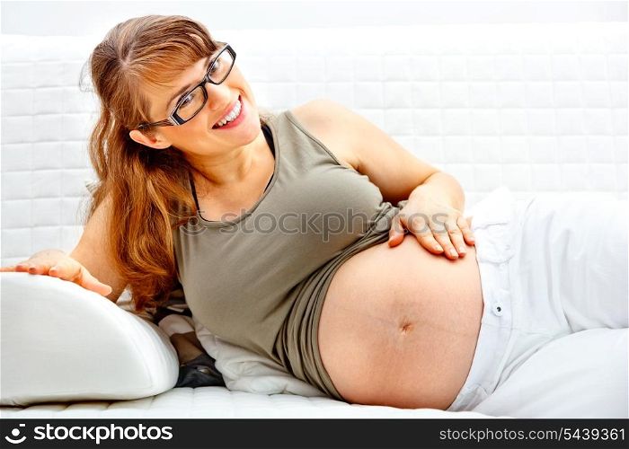 Smiling beautiful pregnant female relaxing on sofa at home and holding her belly.&#xA;
