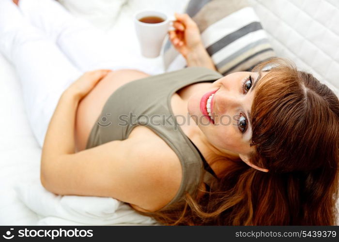 Smiling beautiful pregnant female relaxing on sofa at home with cup of tea in hand. Close-up.&#xA;