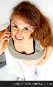 Smiling beautiful pregnant female sitting on sofa at home and talking mobile phone.&#xA;