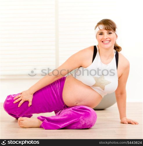 Smiling beautiful pregnant woman doing stretching exercises on floor at home&#xA;