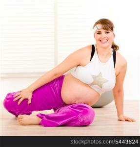 Smiling beautiful pregnant woman doing stretching exercises on floor at home&#xA;