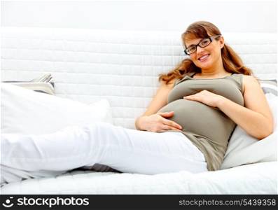 Smiling beautiful pregnant woman lying on sofa at home and holding her belly.&#xA;