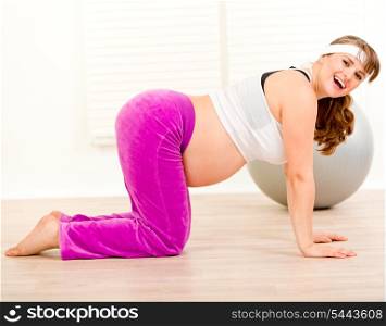 Smiling beautiful pregnant woman making gymnastics at living room&#xA;
