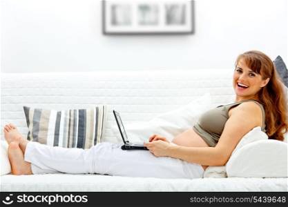 Smiling beautiful pregnant woman on sofa at home with the laptop and a credit card.&#xA;