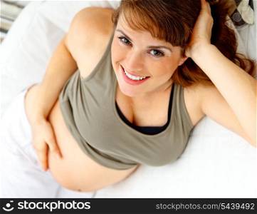 Smiling beautiful pregnant woman relaxing on couch at home and holding her belly.&#xA;